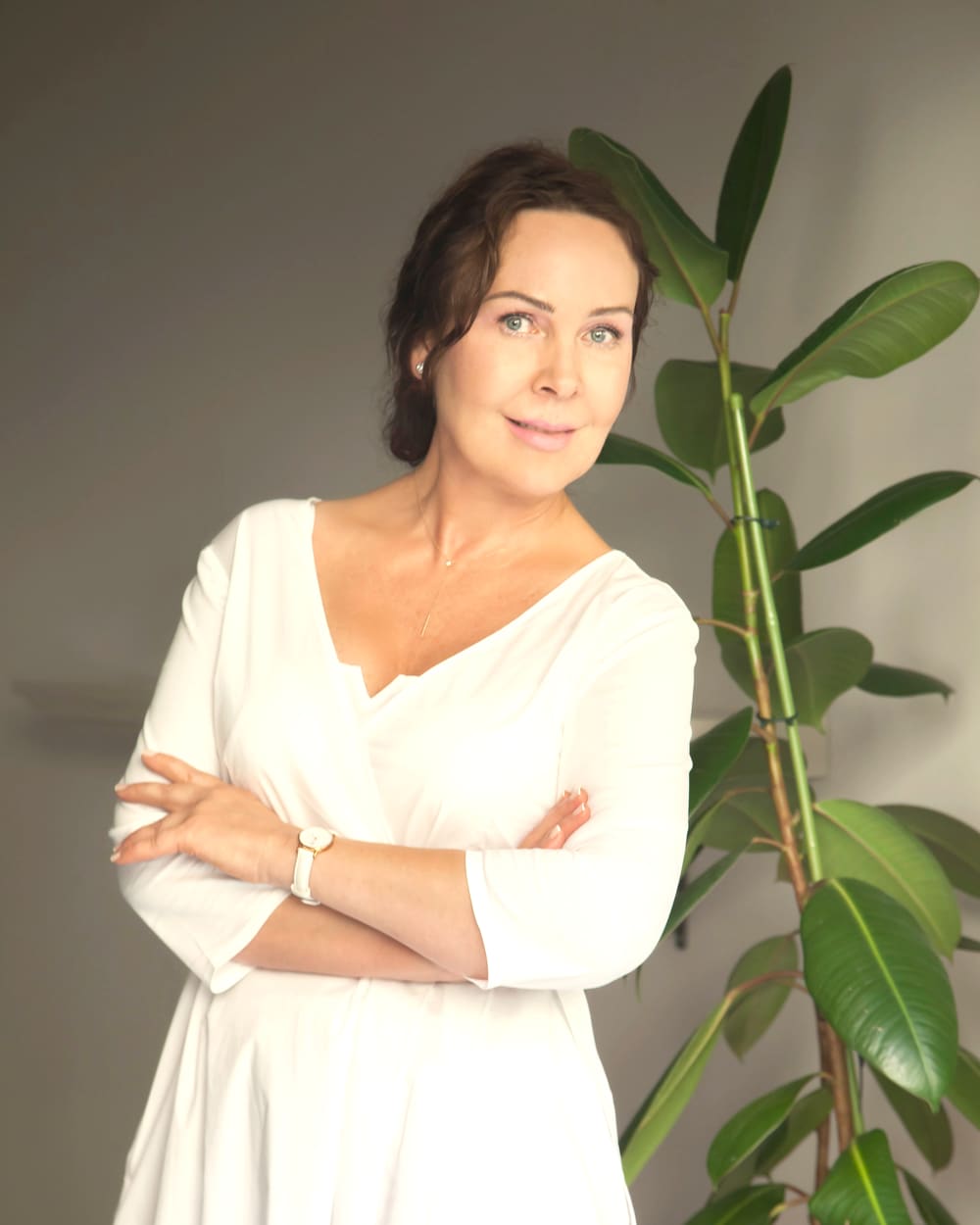 Žana Mitiajeva, dressed in white, standing beside a large house plant